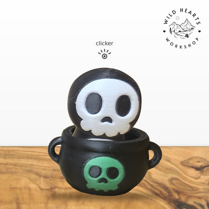 Hooded Skull clicker top (hooded skeleton skull) seated in the black cauldron with green skull base